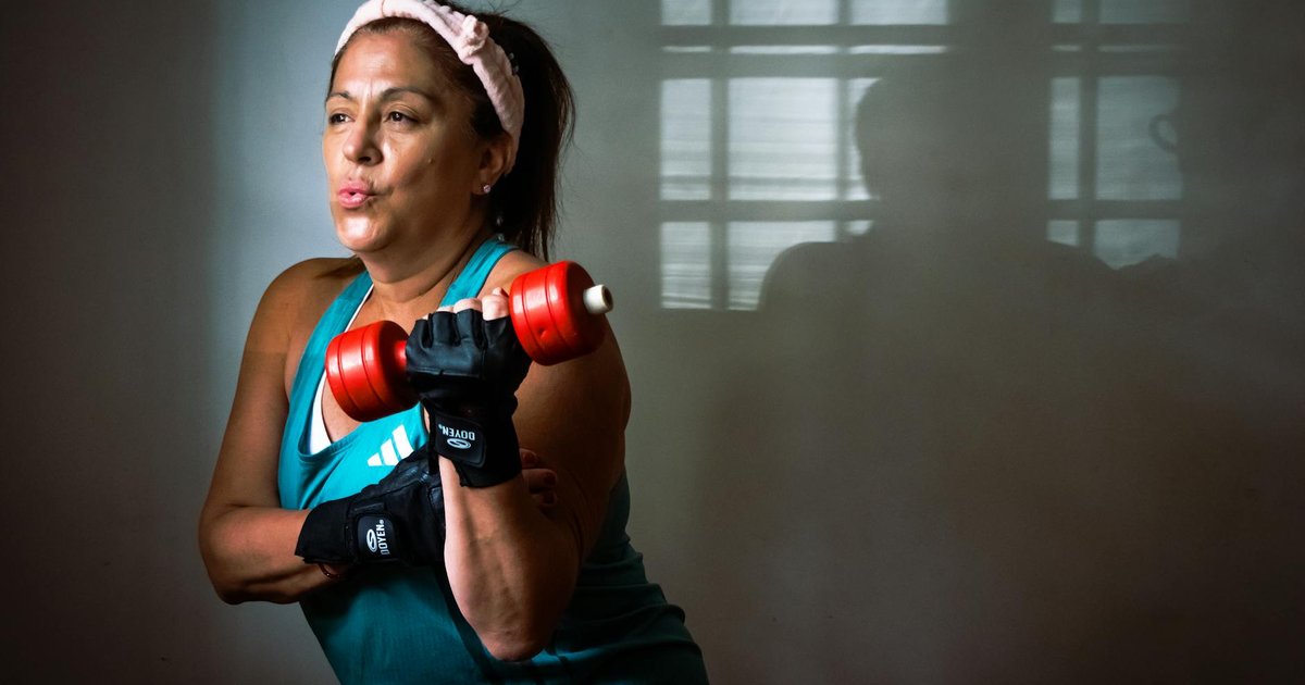 A middle-aged woman exercising indoors with a red dumbbell, showcasing strength and fitness motivation.